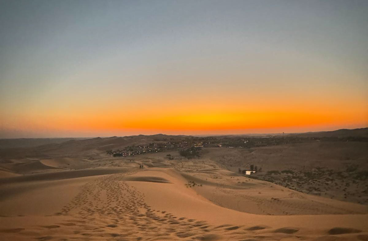 Mystischer Sonnenaufgang über der endlosen Wüste von Abu Dhabi – goldene Dünen erstrecken sich bis zum Horizont, während ein verträumtes Wüstendorf in warmes Licht getaucht wird. Ein exklusives Reiseziel für Luxusreisende, die die Ruhe der Wüste, unvergessliche Abenteuer und authentische arabische Kultur erleben möchten. Buchbar in GErlingen und Stuttgart