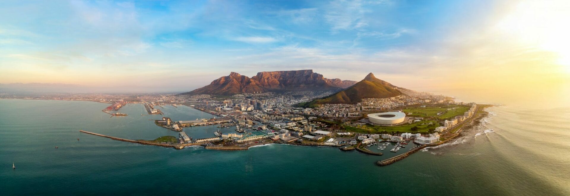 Diese atemberaubende Panoramaaufnahme zeigt Kapstadt, eine der spektakulärsten Metropolen der Welt, eingebettet zwischen dem türkisfarbenen Atlantik und dem majestätischen Tafelberg. Die goldenen Strahlen der untergehenden Sonne tauchen die Stadt in ein warmes Licht und lassen die Küstenlinie sowie das berühmte Stadion erstrahlen. Im Vordergrund erstreckt sich die Victoria & Alfred Waterfront, das pulsierende Herz der Stadt, das Luxus, Shopping und erstklassige Gastronomie vereint. Die historische Hafenanlage mit ihren charmanten Segelbooten trifft hier auf moderne Architektur, was Kapstadt zu einem Magneten für Genießer und Abenteurer macht. Für Reisende, die das Exklusive mit dem Abenteuerlichen verbinden möchten, bietet Kapstadt unvergessliche Erlebnisse: Von einer luxuriösen Safari zu den Big Five, über eine Fahrt entlang des spektakulären Chapman’s Peak Drive, bis hin zu erlesenen Weingütern in Stellenbosch – hier verschmelzen Natur, Kultur und Genuss auf höchstem Niveau. Lass dich von MHS Reisen inspirieren und erlebe Kapstadt mit all seinen Facetten – buchbar in Gerlingen und Stuttgart!