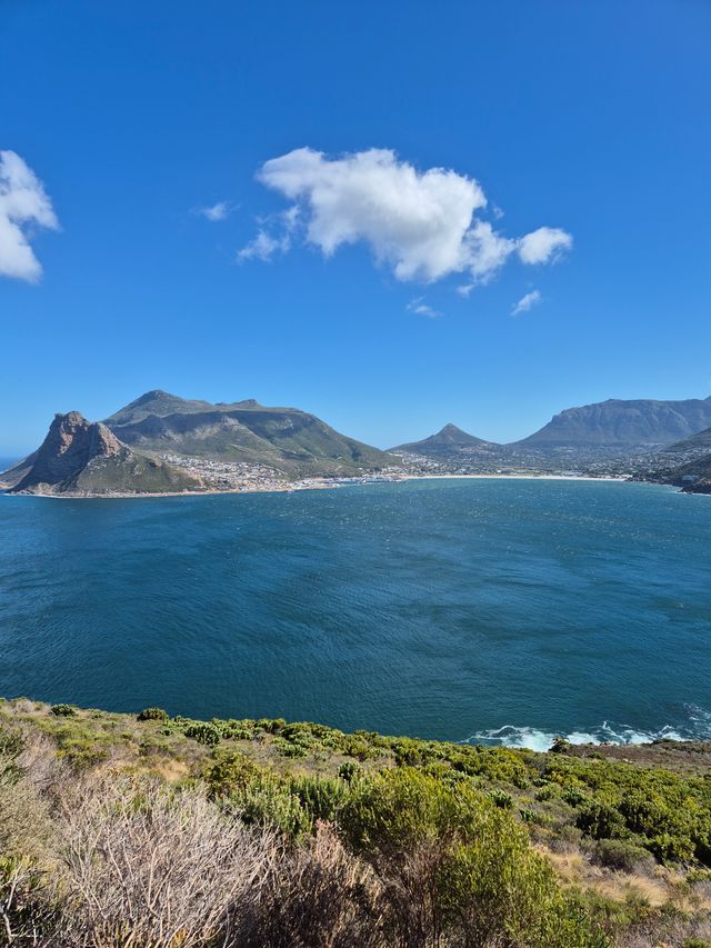 Dieses beeindruckende Panorama zeigt die malerische Hout Bay in Südafrika, eingefasst von der atemberaubenden Kulisse der Berge entlang des legendären Chapman’s Peak Drive. Der tiefblaue Atlantik erstreckt sich vor der dramatischen Küstenlandschaft, während die sattgrünen Hügel im Vordergrund den Blick auf eine der spektakulärsten Routen der Welt freigeben. Die Kontraste zwischen dem azurblauen Himmel, den weißen Sandstränden und den majestätischen Bergformationen verleihen dieser Szene eine fast surreal anmutende Schönheit. Ein einzelnes, fluffiges Wölkchen schwebt über der Landschaft und verstärkt die Ruhe und Weite dieses Naturparadieses. Südafrika in seiner vollen Pracht! 🌍✨ Hout Bay und der berühmte Chapman’s Peak Drive bieten einen unvergesslichen Mix aus wilder Natur, türkisfarbenem Ozean und imposanten Berglandschaften. Ob als Teil eines Luxus-Roadtrips entlang der Garden Route oder als Zwischenstopp auf dem Weg nach Kapstadt – diese atemberaubende Bucht ist ein absolutes Highlight. Sichere dir jetzt dein exklusives Südafrika-Erlebnis und buche deine Traumreise direkt bei uns in Gerlingen oder Stuttgart.