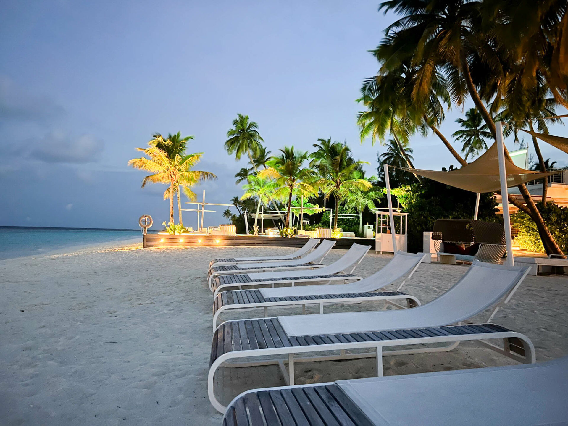 Luxuriöser Sandstrand auf den Malediven in der Abenddämmerung, mit stilvollen Liegen unter Palmen und sanfter Beleuchtung. Die perfekte Kulisse für einen exklusiven Traumurlaub mit Entspannung, tropischem Flair und atemberaubendem Meerblick – ideal für Luxusreisende, die Ruhe und Komfort suchen Paradies buchbar in Stuttgart und gerlingen.