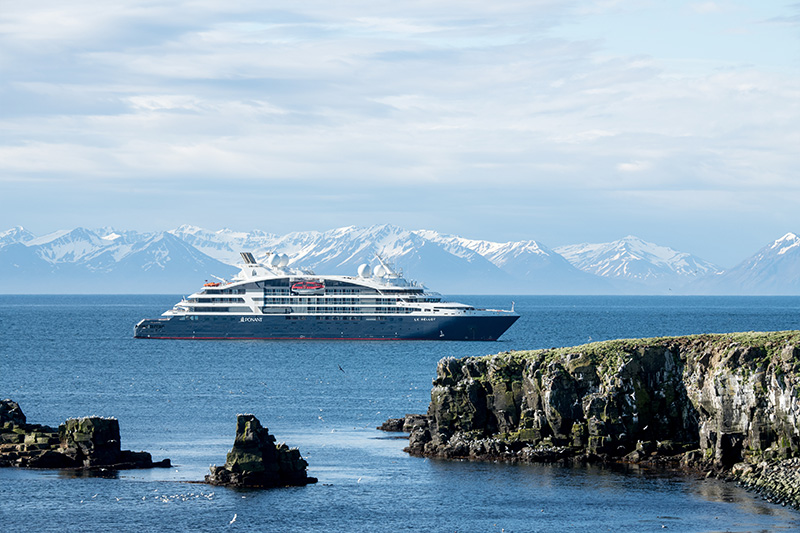 Das luxuriöse Expeditionskreuzfahrtschiff von Ponant liegt auf Reede vor einer atemberaubenden Kulisse aus schroffen Klippen und schneebedeckten Bergen. Ein exklusives Reiseerlebnis für Entdecker, die abgelegene Regionen, eisige Landschaften und unvergessliche Abenteuer auf See genießen möchten.